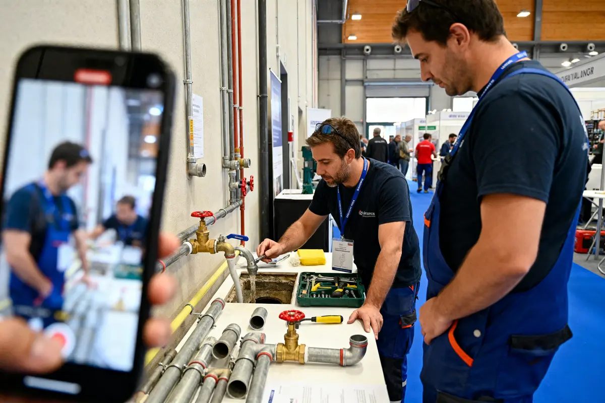 Professionnels travaillant sur des tuyaux à l'événement de plomberie, photographiés par un smartphone