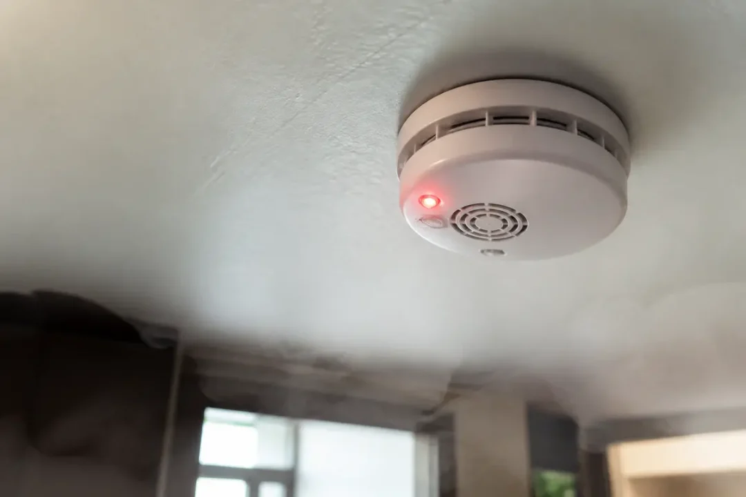 Un détecteur de fumée fixé au plafond, émettant un signal lumineux rouge.