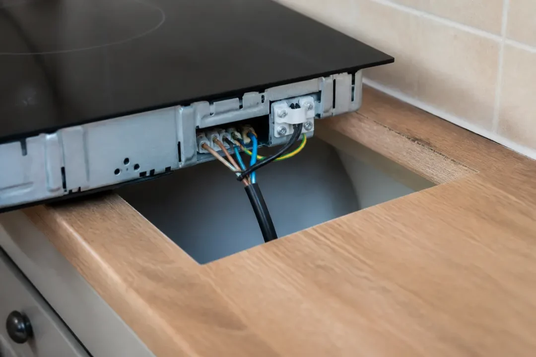 Plaque de cuisson partiellement intégrée dans un plan de travail en bois, avec câbles électriques visibles.