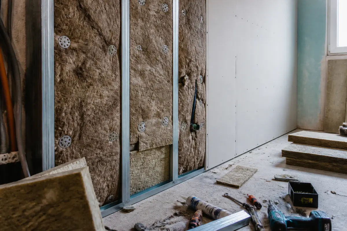 Cloison en construction avec isolation acoustique, profilés métalliques, plaques de plâtre et outils au sol.