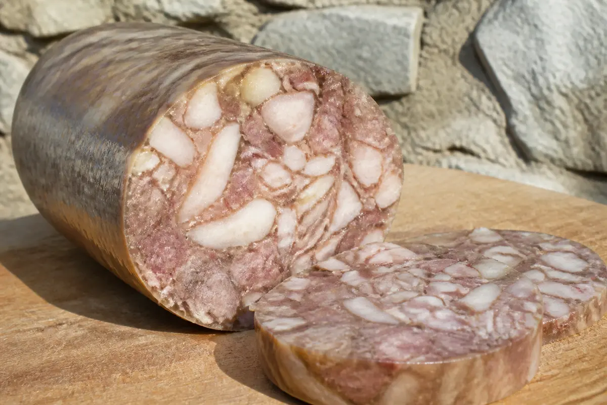 Saucisson artisanal tranché, posé sur une planche en bois, avec un mur de pierres en arrière-plan.