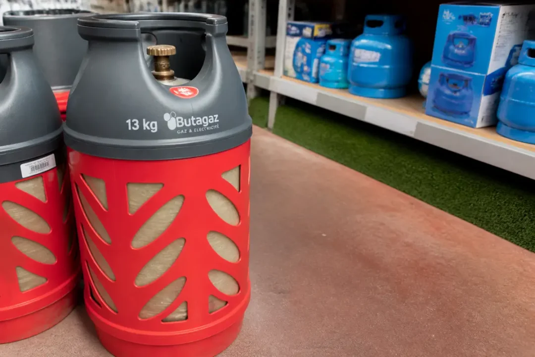 Bouteilles de gaz Butagaz rouges sur étagère de magasin, fond de bouteilles bleues.