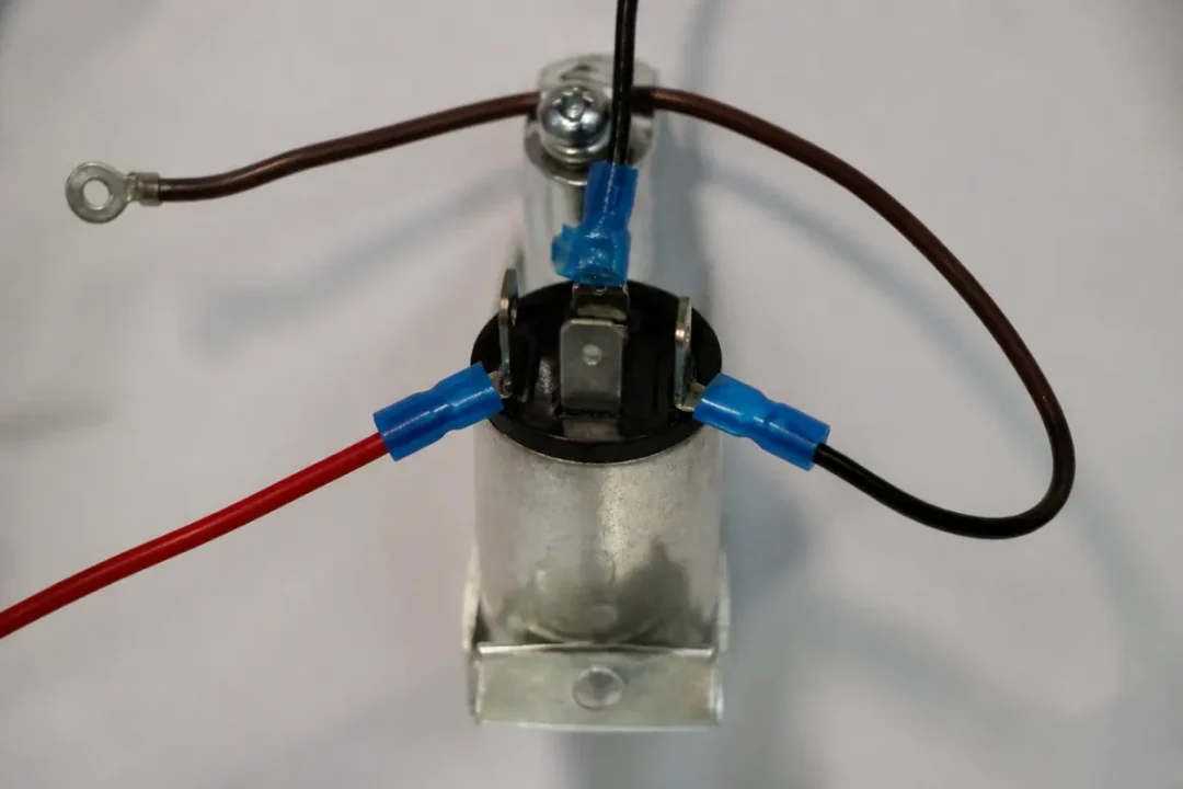 Connecteurs électriques bleu sur un cylindre métallique, avec fils rouge et noir, fixés en haut.